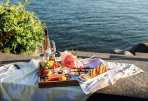 Picknickbricka med frukt, grönsaker och vin vid vattnet